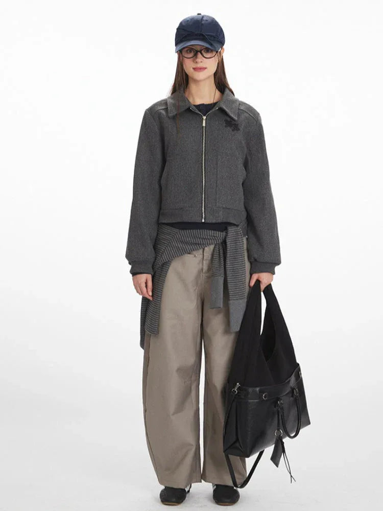 Woman wearing a grey cropped bomber jacket with a zipper closure and collared neckline, paired with beige wide-leg pants and a black handbag. Main image