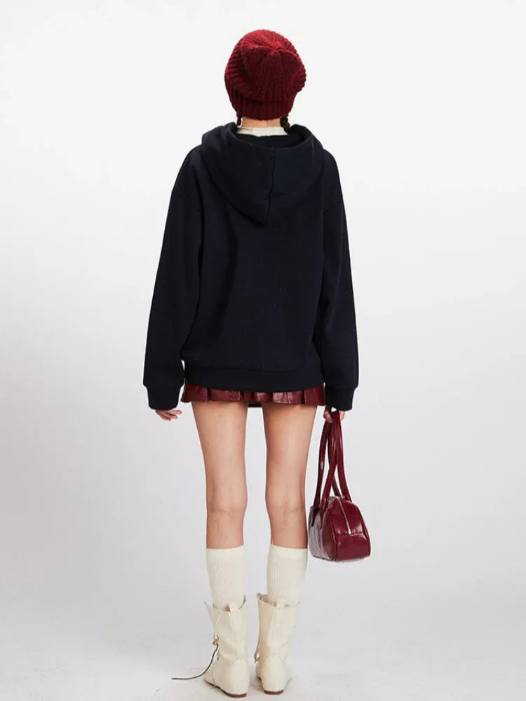 Back view of a woman wearing a navy blue hooded fleece jacket with apple-shaped buttons.