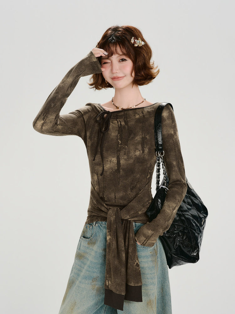 Woman wearing a long-sleeve brown tie-front top with a tie-neck detail and acid wash effect, paired with light-wash wide-leg jeans.