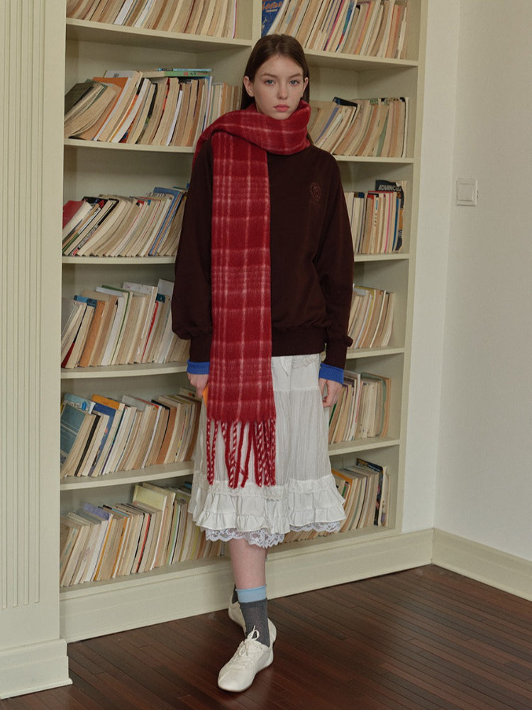 Woman wearing a white long-sleeved shirt, white pleated skirt, grey polka dot tights, silver boots, and a grey plaid scarf with fringe.