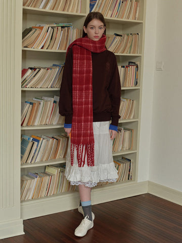 Woman wearing a white long-sleeved shirt, white pleated skirt, grey polka dot tights, silver boots, and a grey plaid scarf with fringe.