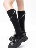 Close-up of black knee-high socks with silver stud detailing and a strap, paired with platform shoes.