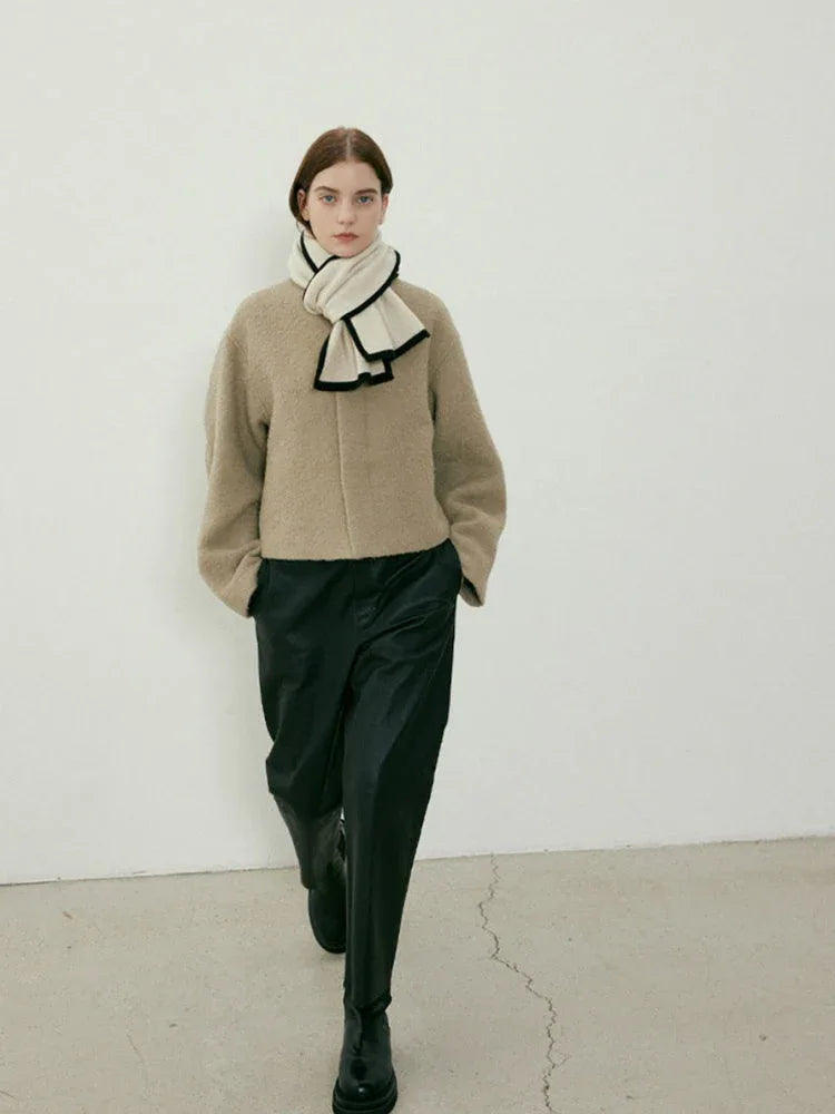Model walking in a tan jacket and black pants, wearing a cream and black scarf