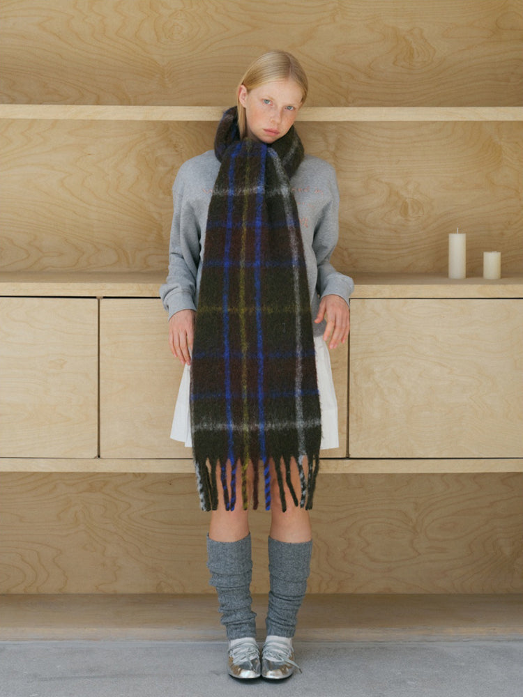 Model showcasing a dark green and blue plaid scarf with fringe.