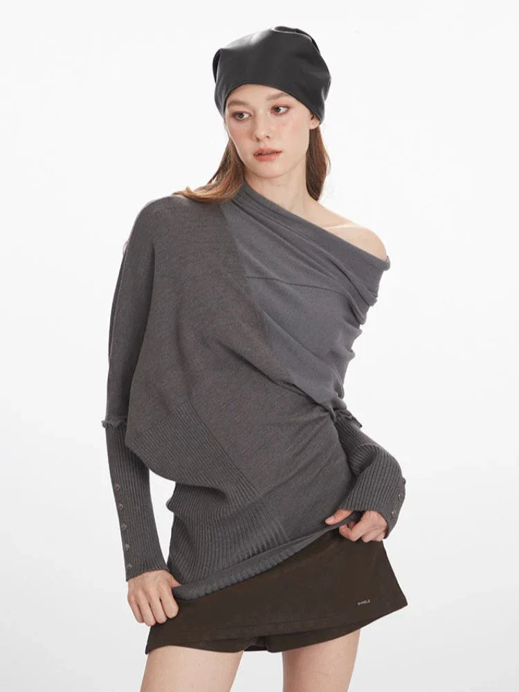Woman demonstrating the fit and details of a grey asymmetrical knit sweater with draped overlay.