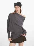 Woman demonstrating the fit and details of a grey asymmetrical knit sweater with draped overlay.
