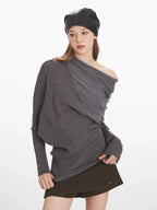 Woman demonstrating the fit and details of a grey asymmetrical knit sweater with draped overlay.