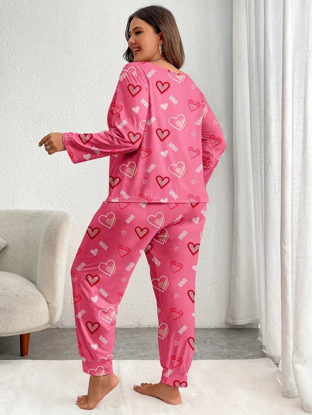 Woman wearing a pink long-sleeved pajama set with an all-over heart print, showing the back view.