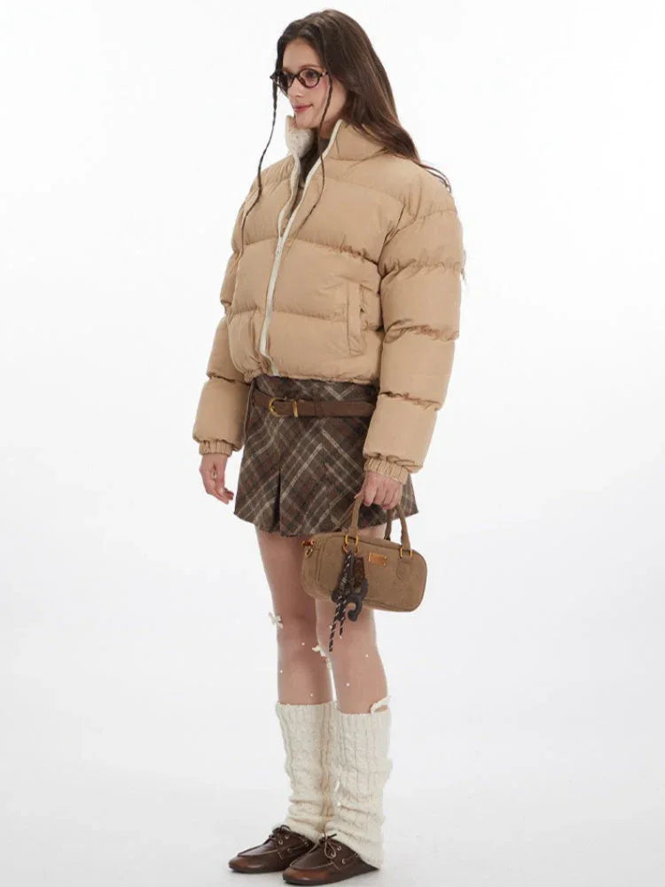 Woman wearing a beige cropped puffer jacket with a white zipper and stand-up collar.