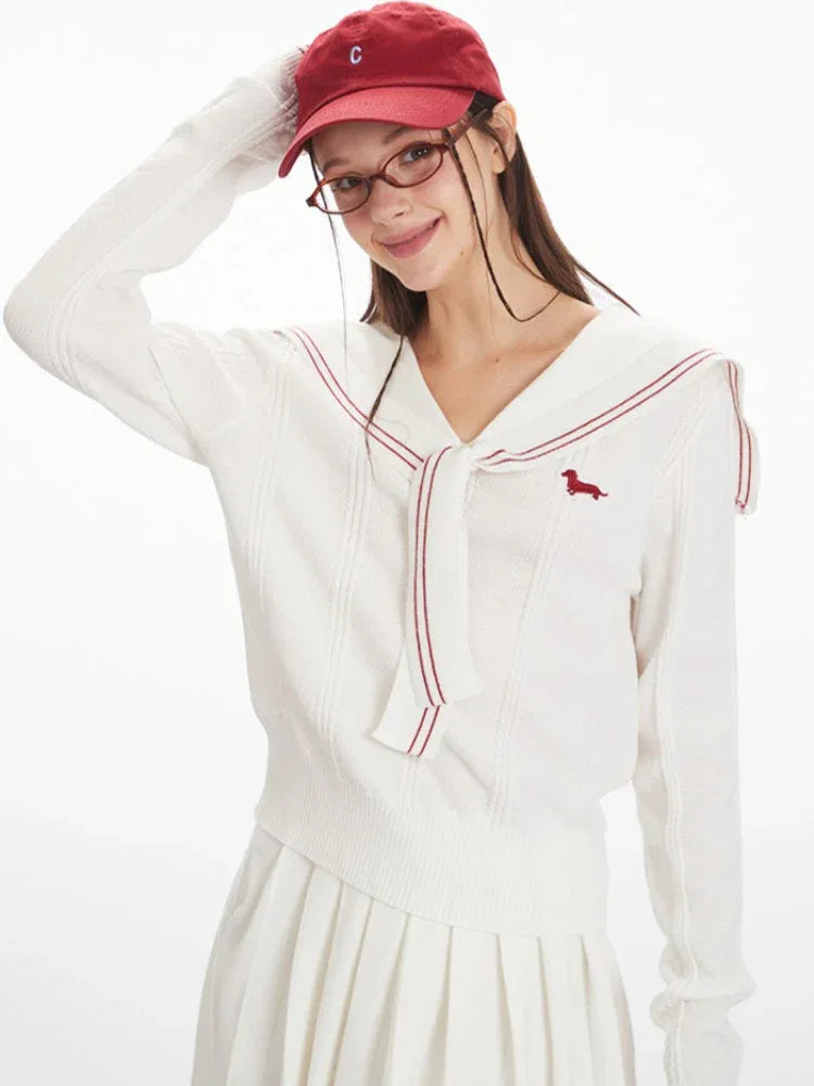 Close-up of a woman wearing a white knit sweater with a navy sailor collar and red trim, and a red embroidered dachshund graphic.