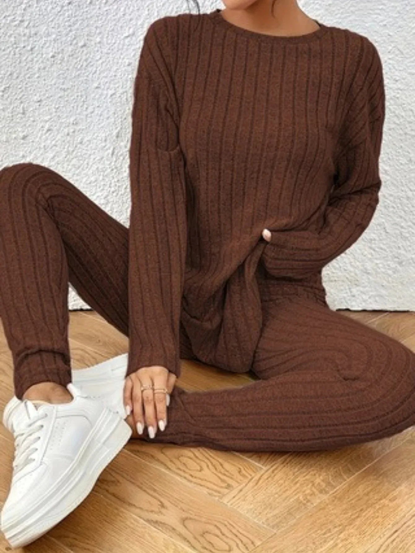Close-up of a woman's torso and legs wearing a brown ribbed knit loungewear set with a crew neck top and slim-fit pants, seated on the floor.