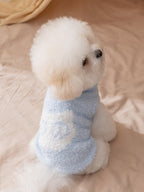 Side view of a white bichon frise dog wearing a light blue fluffy dog sweater with a white "Wcat" logo patch.