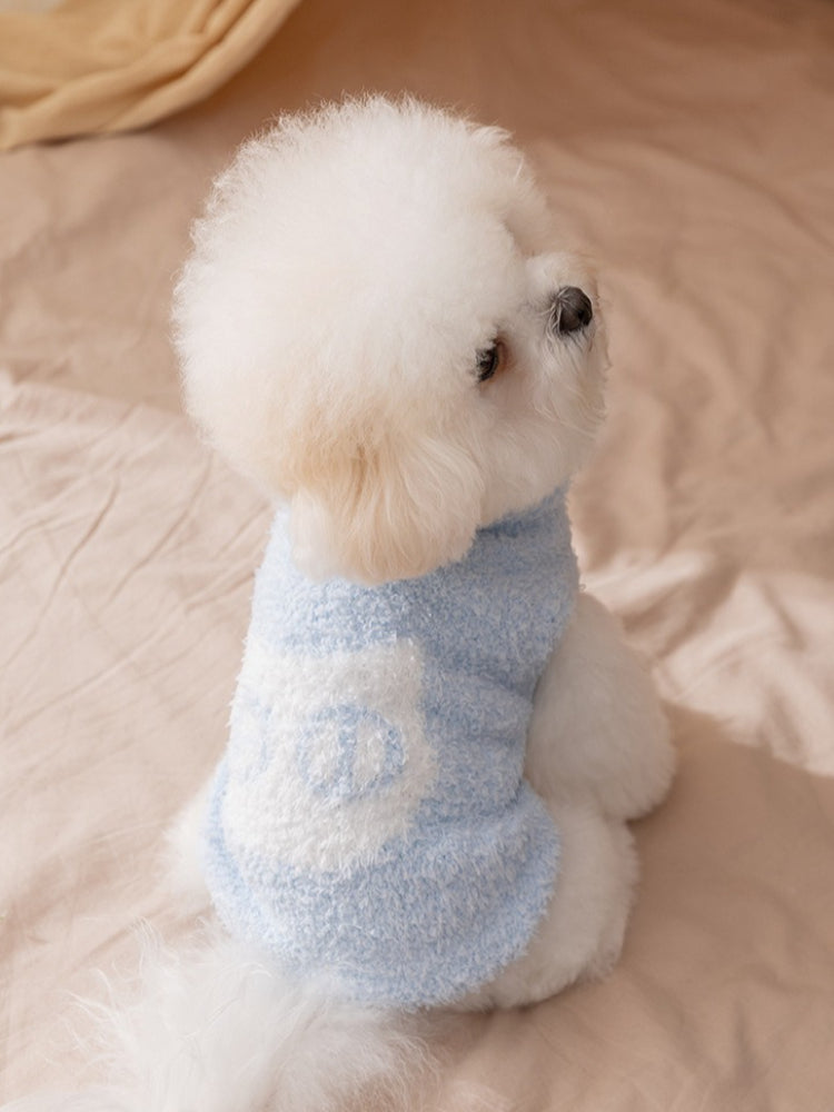 Side view of a white bichon frise dog wearing a light blue fluffy dog sweater with a white "Wcat" logo patch.