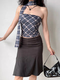 Full body shot of a woman in a plaid tube top and skirt, holding a black handbag.