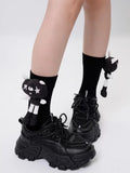 Close-up of black crew socks featuring a black and white cartoon cat applique on each sock, paired with black platform sneakers.