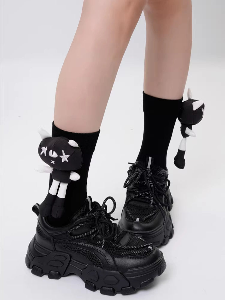 Close-up of black crew socks featuring a black and white cartoon cat applique on each sock, paired with black platform sneakers.