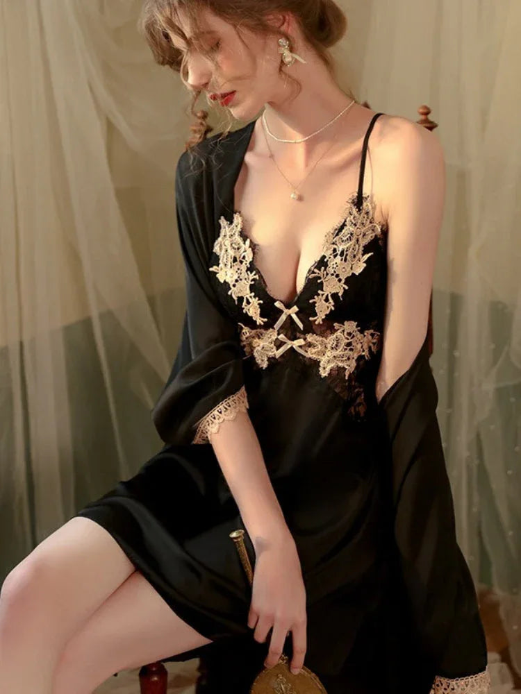 Woman wearing a black satin slip dress with lace detailing and a matching robe, seated.