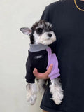 Person holding a miniature schnauzer wearing a black and purple dog onesie.