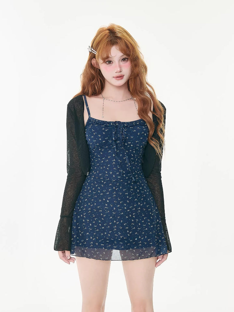 Woman wearing a navy floral print mini dress with spaghetti straps and a tie-front detail, paired with a sheer black cardigan and brown boots.