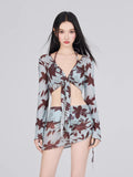 Woman wearing a light blue and brown floral print sheer long-sleeve tie-front cropped top with a matching ruched mini skirt.