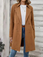 Woman wearing a brown suede-like longline coat with a notched lapel and double-breasted button closure.