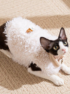 A black and white cat wearing a white faux fur coat lying down.