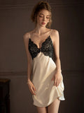 Woman wearing a cream-colored satin slip dress with black lace trim, standing.