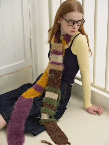 Woman wearing a striped fuzzy scarf with multi-colored stripes in purple, yellow, and brown, sitting on the floor.