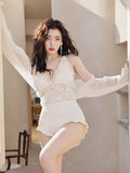 Woman posing in a white lace swimsuit and sheer cover-up, with her arms extended.