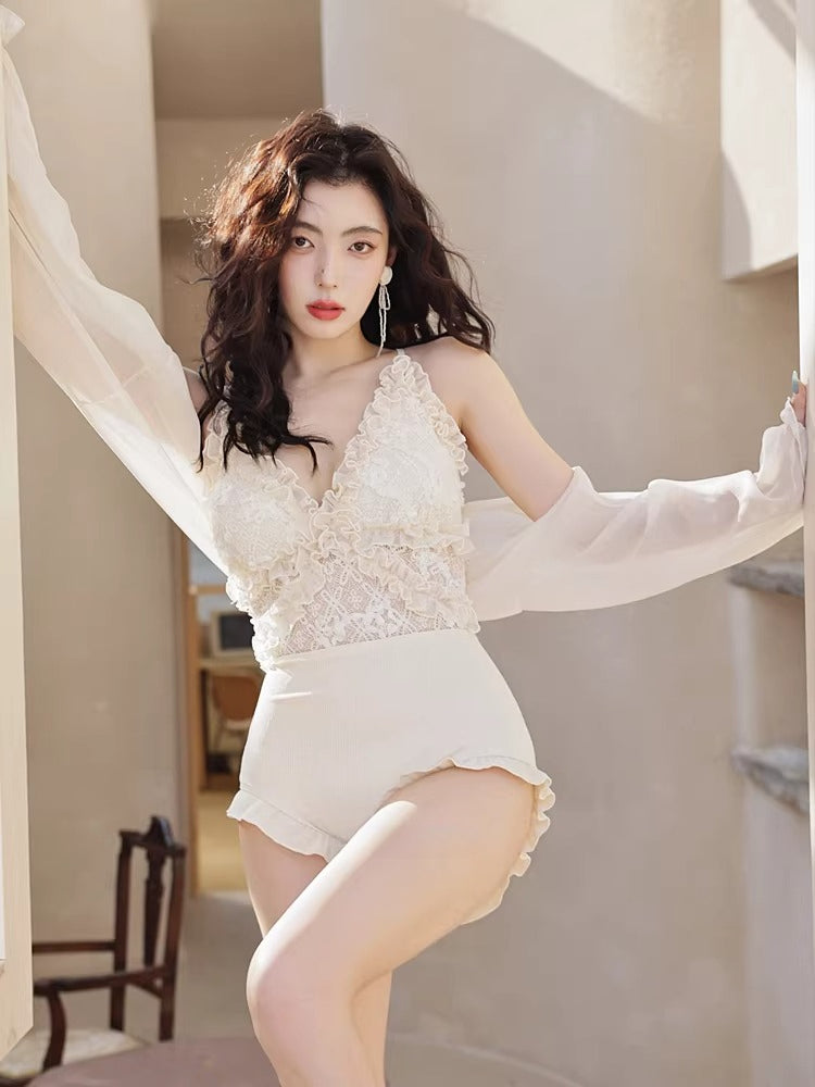 Woman posing in a white lace swimsuit and sheer cover-up, with her arms extended.