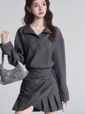 Woman holding a silver handbag while wearing a grey top and skirt