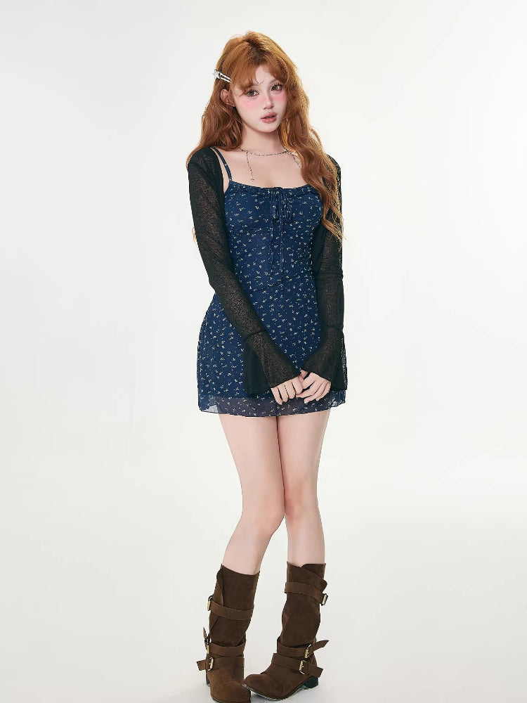 Full body shot of a woman wearing a navy floral print mini dress with spaghetti straps and a tie-front detail, layered with a sheer black cardigan and brown boots.