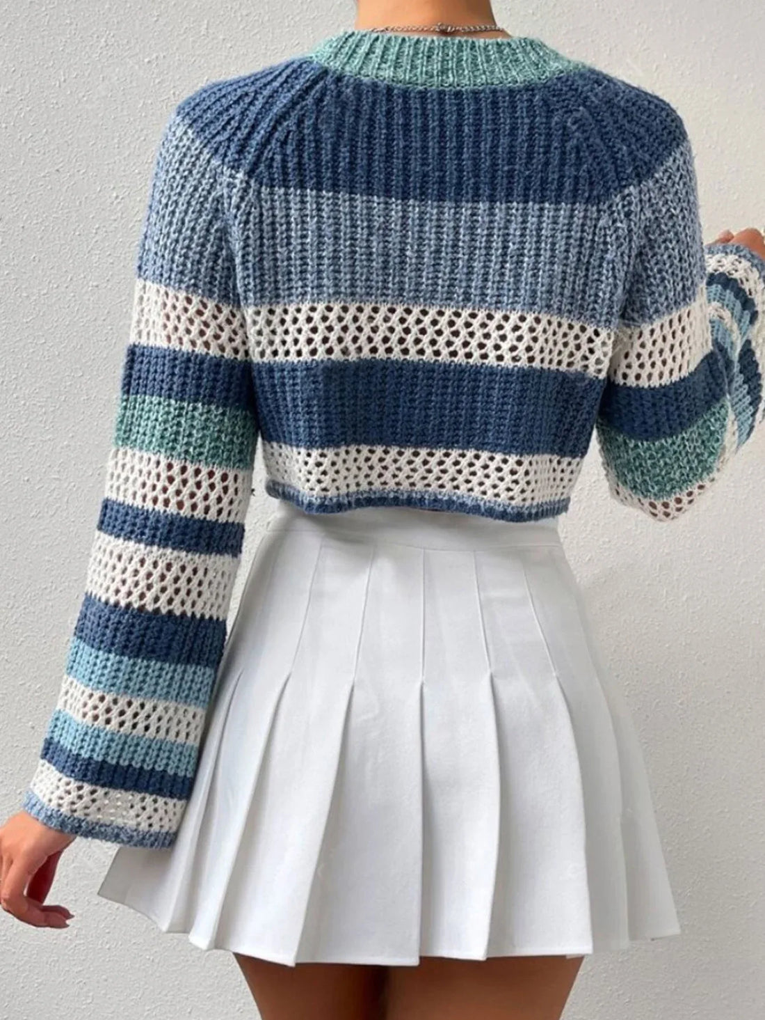 Woman wearing a blue, white, and green striped crochet knit cropped sweater with bell sleeves.