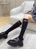 Woman wearing black knee-high socks with a black buckle strap detail and black platform loafers.