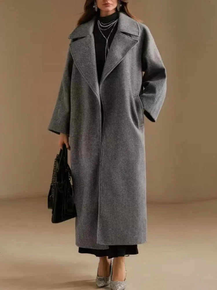 Woman wearing a long grey wool blend coat with oversized lapels and drop shoulder sleeves.