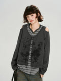 Woman wearing a dark gray graphic print cropped long-sleeve top with cold shoulder cutouts and a lace-up front over a gray and white striped t-shirt.