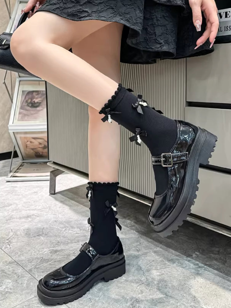 Full view of black ankle socks with decorative bows and pearls, alongside black platform mary jane shoes with a buckle strap