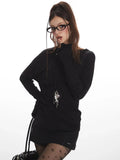 Model posing with a hand near her face, highlighting the black long-sleeved top and accessories.