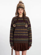 Close-up front view of a woman modeling a striped knit sweater with decorative pom-poms.