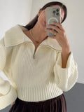 Close-up of a woman taking a selfie in a cream-colored knit sweater with a half-zip neckline.
