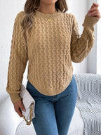 Woman in a tan knit sweater and blue jeans holding a white clutch bag.