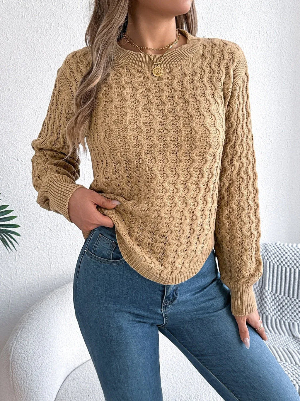 Woman wearing a tan textured knit sweater with a crew neckline and long sleeves, paired with blue jeans.