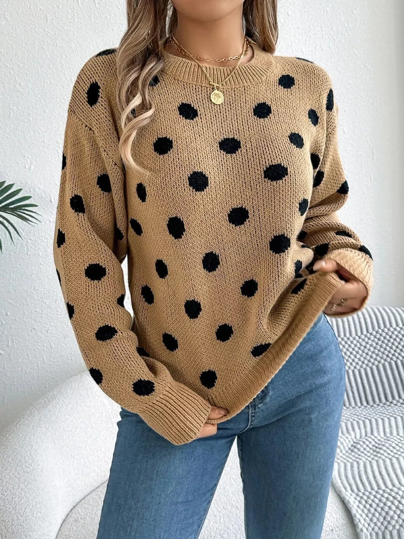 Woman wearing a tan knit sweater with a black polka dot pattern, long sleeves, and a crew neckline.
