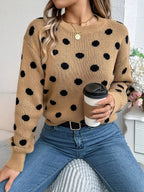 Woman holding a coffee cup while wearing a tan polka dot sweater and blue jeans.