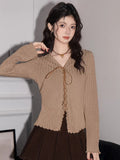 Woman wearing a tan ribbed knit long-sleeve top with a lace-up v-neck and scalloped hem
