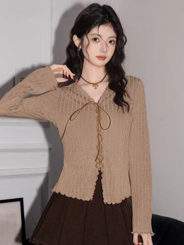 Woman wearing a tan ribbed knit long-sleeve top with a lace-up v-neck and scalloped hem