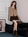 Full body shot of a woman in a tan ribbed knit long-sleeve top, brown pleated skirt, and brown boots