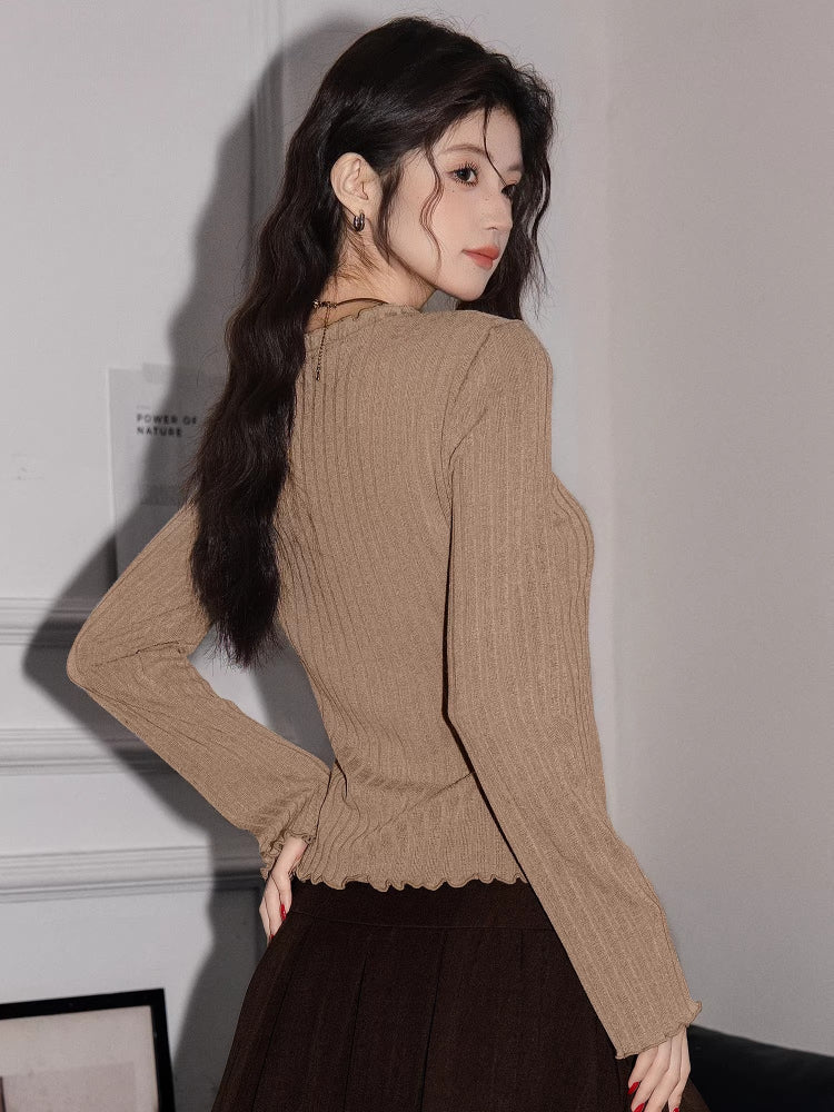 Woman wearing a tan ribbed knit long-sleeve top with a lace-up v-neck and scalloped hem