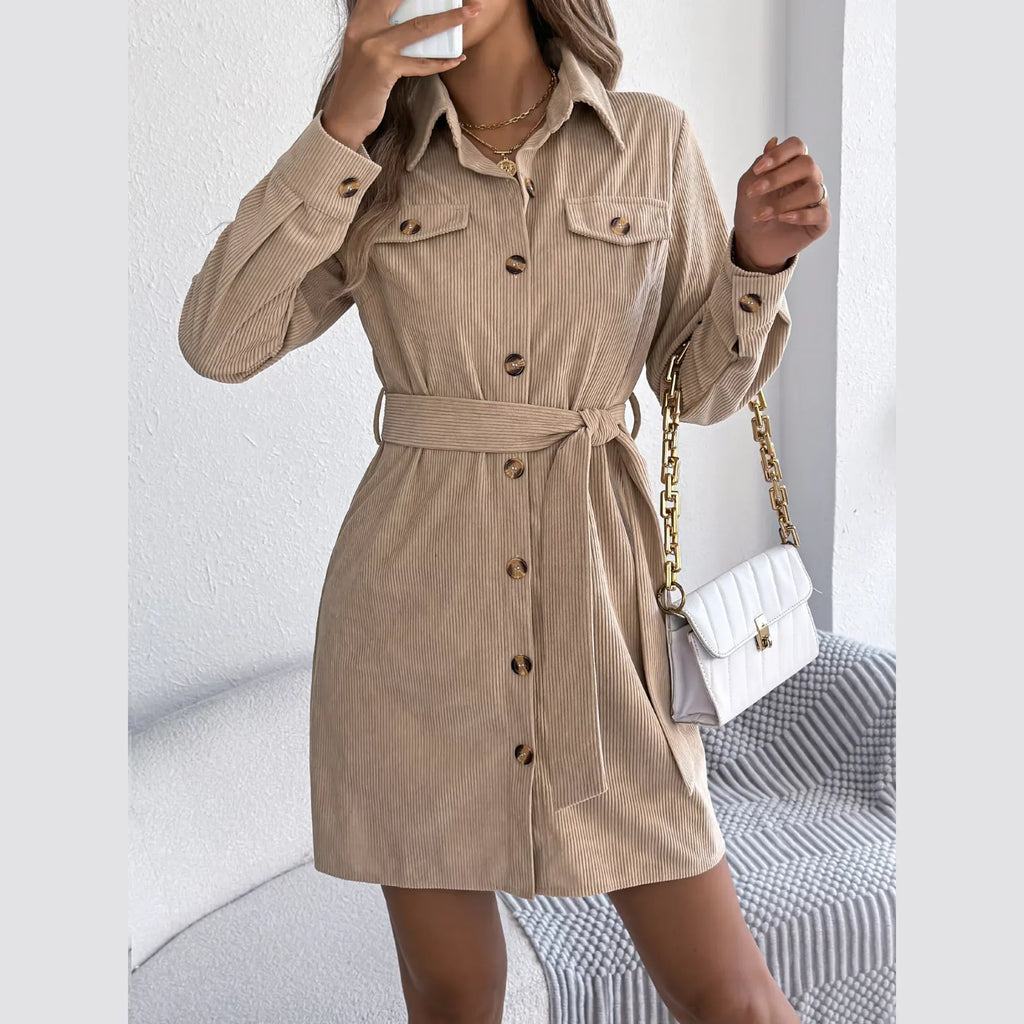 Woman holding a white handbag and a phone while wearing a beige corduroy shirt dress.