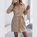 Woman holding a white handbag and a phone while wearing a beige corduroy shirt dress.